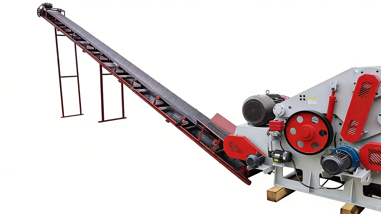 Vista lateral detalhada de um grande sistema industrial de picagem de madeira, focando na interface entre a extensa esteira de alimentação inclinada e o picador de tambor com corpo cinza, que apresenta polias vermelhas e correias de transmissão proeminentes.