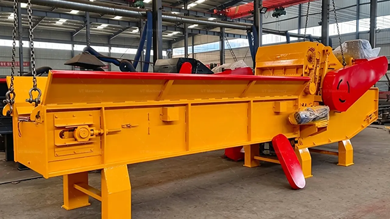 Um potente picador de madeira industrial, com uma estrutura principal amarela vibrante e detalhes marcantes em vermelho, pronto em um grande galpão de fábrica. Sua robusta unidade de processamento, o motor de grande porte e a resistente esteira transportadora de alimentação por corrente definem sua capacidade para trabalho pesado e picagem de alto volume.